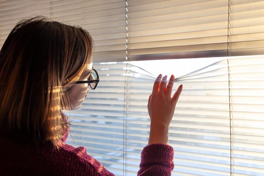 Mujer mirando a través de persiana